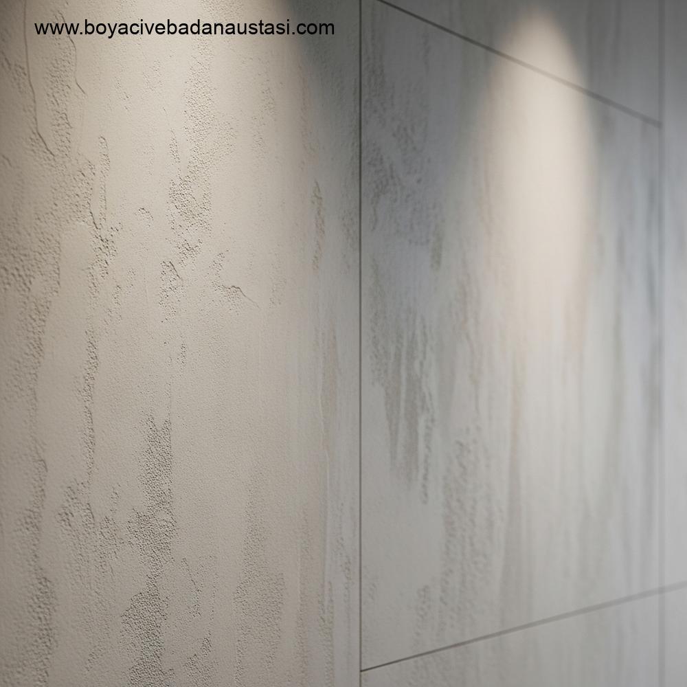 İzmir'de modern bir dairenin iç mekanında, mikrosünger ile beton efektli duvar kaplamasının yakından çekilmiş fotoğrafı. Duvar, mikro çimento kullanılarak tasarlanmış olup, dokuda ve açık gri tonlarda ince varyasyonlar sergilemektedir. Işık yumuşak ve ambiyans odaklıdır, mat ve dokunsal yüzeyi vurgular.